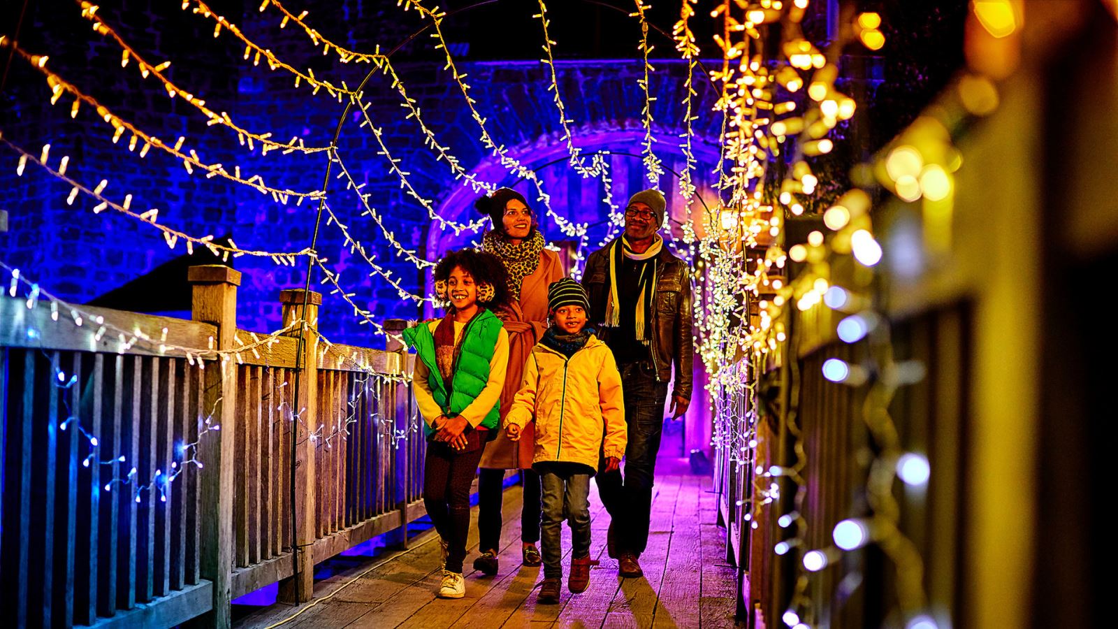 Family walking across bridge with Christmas lights around them 